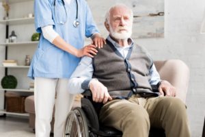 Elderly man in wheelchair with nurse behind them