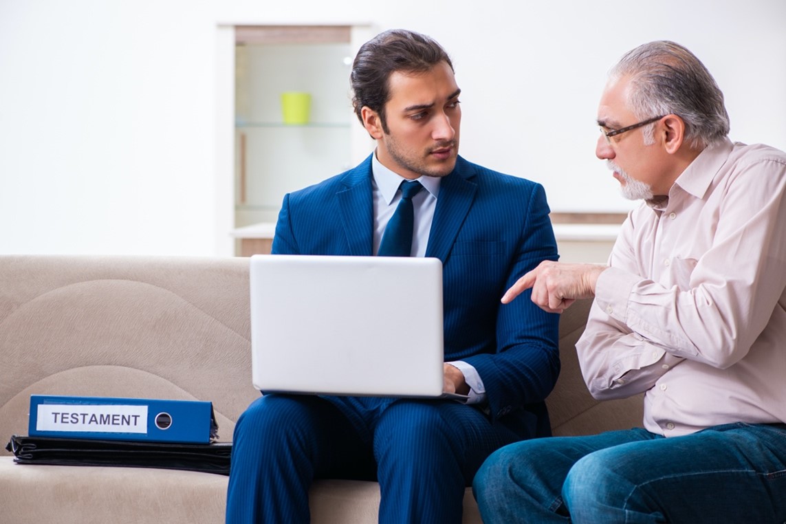A senior in casual attire discusses estate documents with a suited attorney in an informal setting.