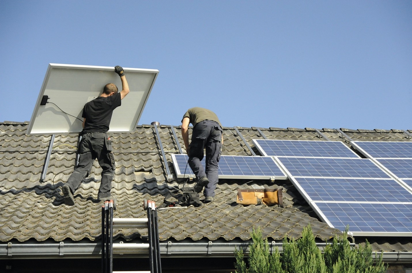 Two workers installing photovoltaic/solar panels on a tiled roof.