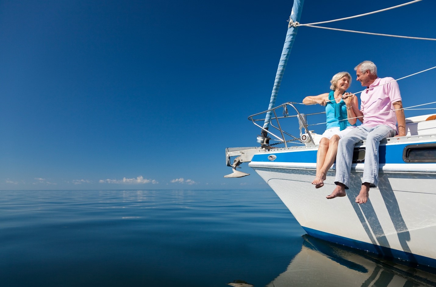 A senior couple sitting barefoot on the side of a yacht.