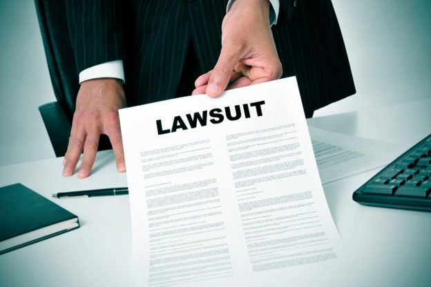 A man in a business suit holds out a sheet of paper with the word LAWSUIT written in capital letters across the top.